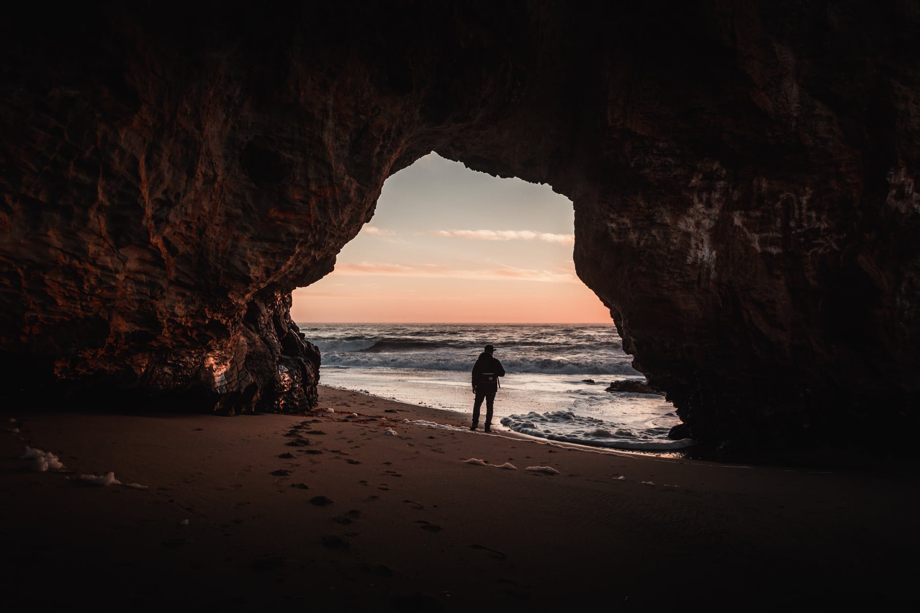 person standing at the entrance of the cave on shore
